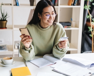 young woman in green sweatshirt looking at phone and credit card