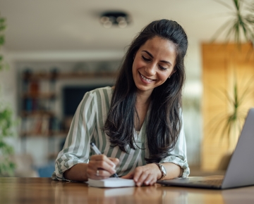 woman writing on notepad with laptop to the side