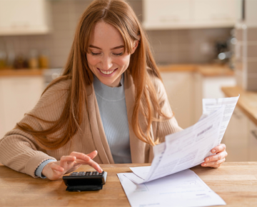 woman at kitchen table looking at papers and calculator