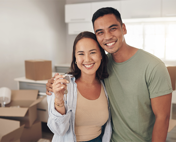 couple with moving boxes in living room holding up keys