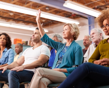 woman raising hand at town hall meeting
