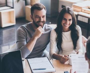 couple talking to someone at desk with paper in front of them