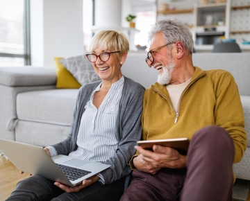 couple with tablet and laptop sitting on floor by couch