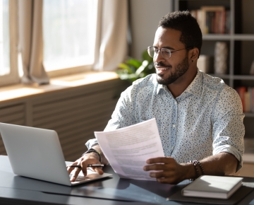 man looking at laptop with papers in his hand