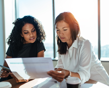 women looking at papers in office with big window in back