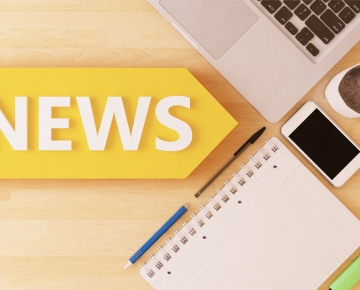 laptop, coffee, phone, notebook, pens, and news sign on desk