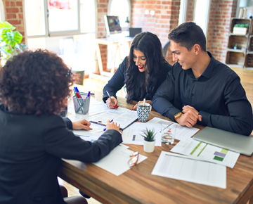 couple wearing black signing papers at desk with mortgage lender wearing black