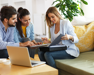 woman in light blue blazer and laptop discussing paperwork with couple on couch